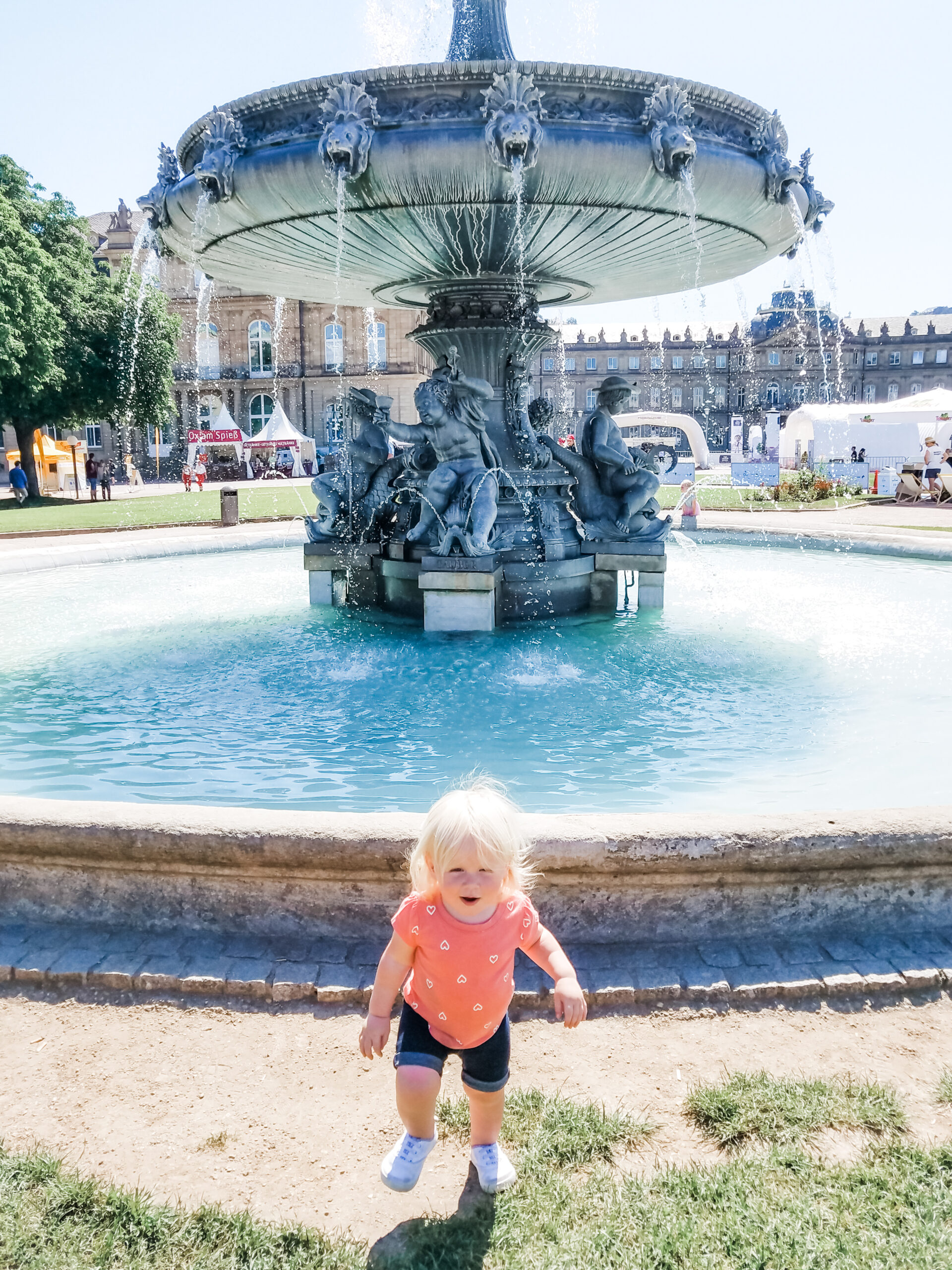 blonde toddler playing in front of large European fountain